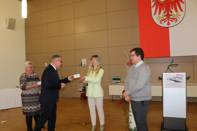 Herr Grieger, Abteilungsleiter 1 im MIK, übergiebt ein kleines Geschenk an AbsolventInnen